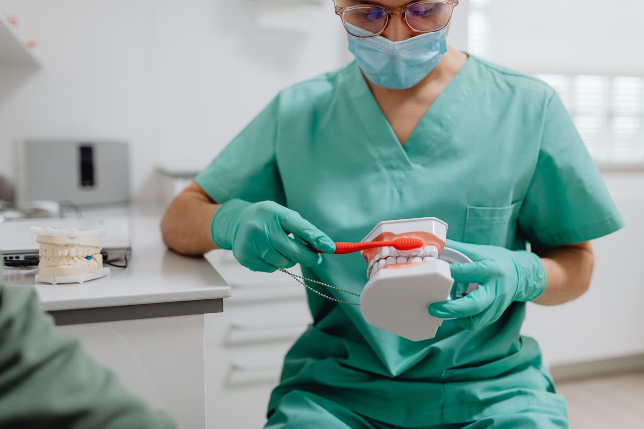 Dental professional in scrubs demonstrates proper brushing on a model in a clinic setting.